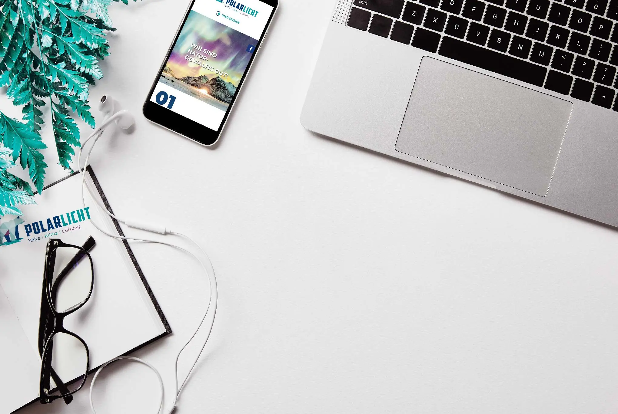 Laptop, Smartphone mit geöffneter Webseite, Brille, Kopfhörer und Pflanze auf weißem Schreibtisch